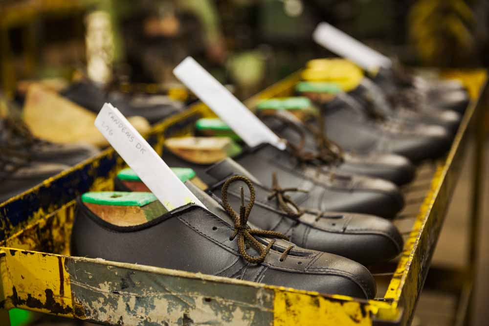 Proses produksi sepatu di pabrik, sepatu kulit hitam yang sedang dalam tahap penyelesaian dengan label produksi.