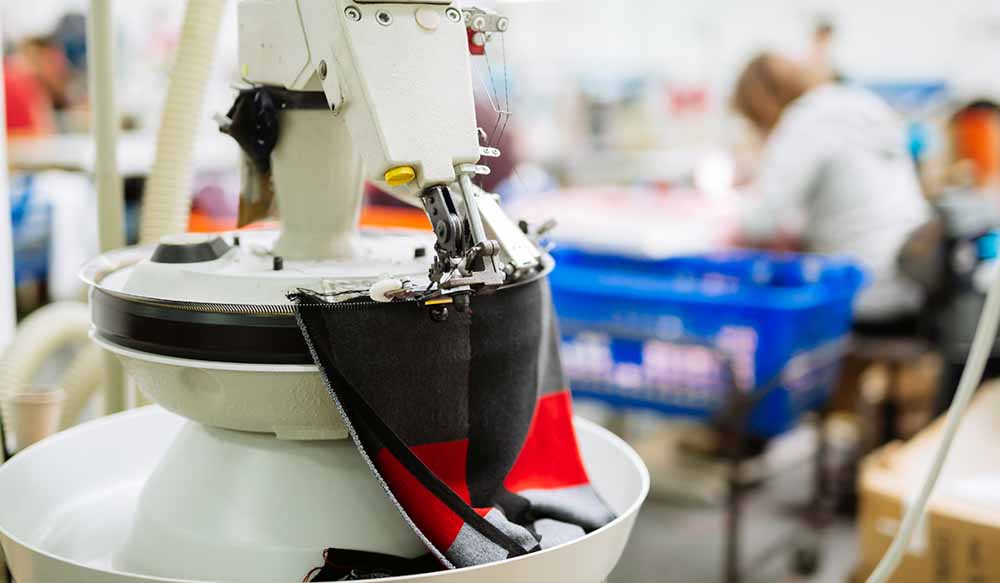 Industrial sewing machine stitching fabric in a footwear factory.