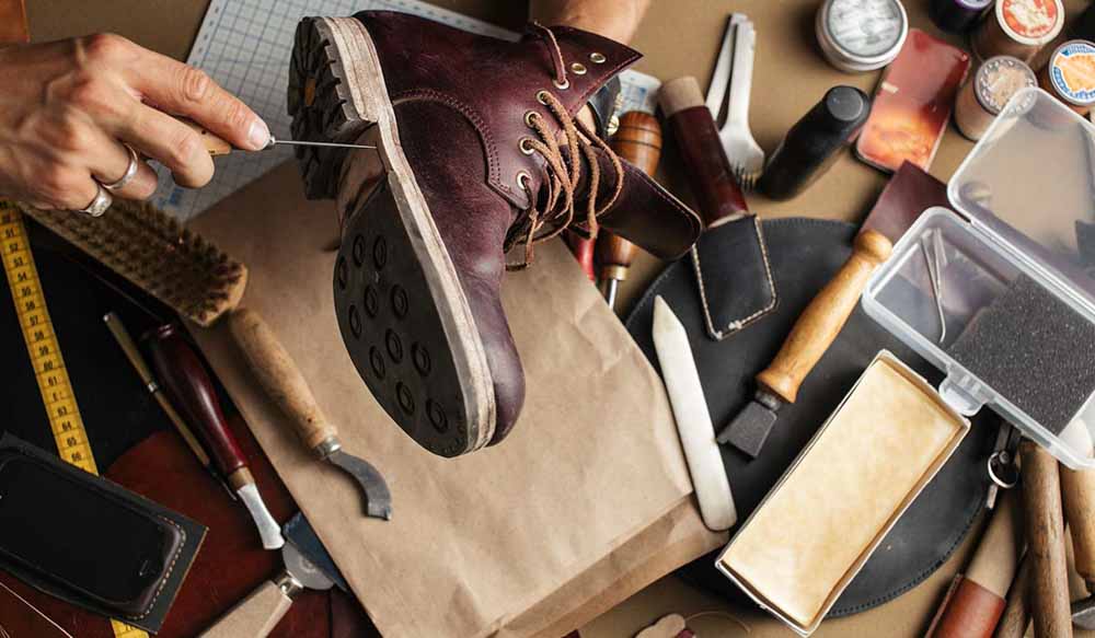crafting a leather boot with shoemaking tools on a work table.