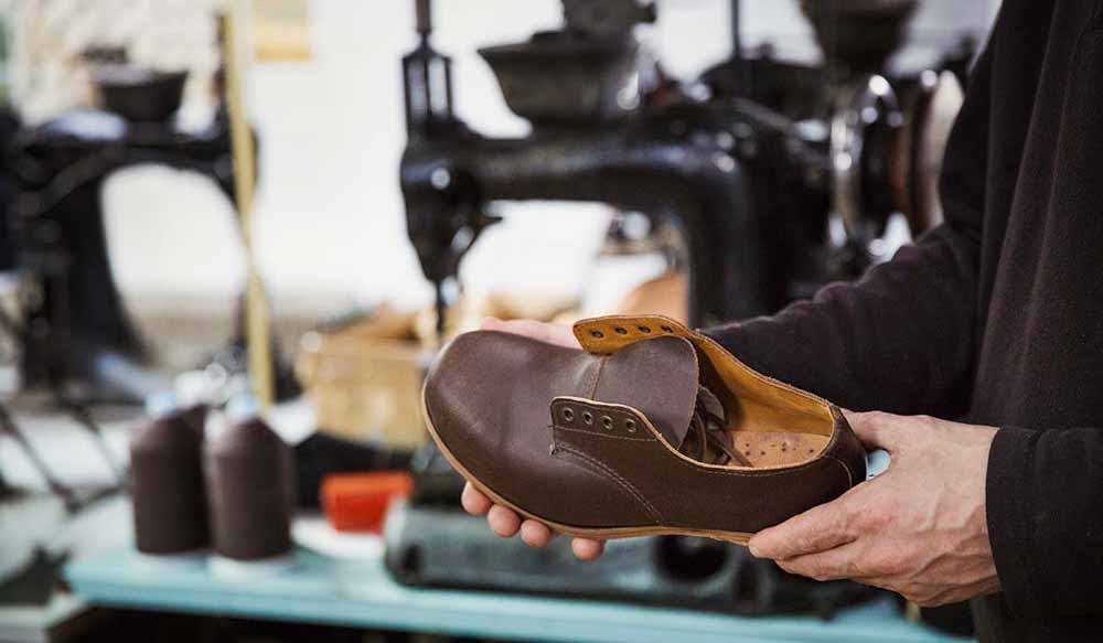 Shoemaker holding a brown leather shoe in a workshop.