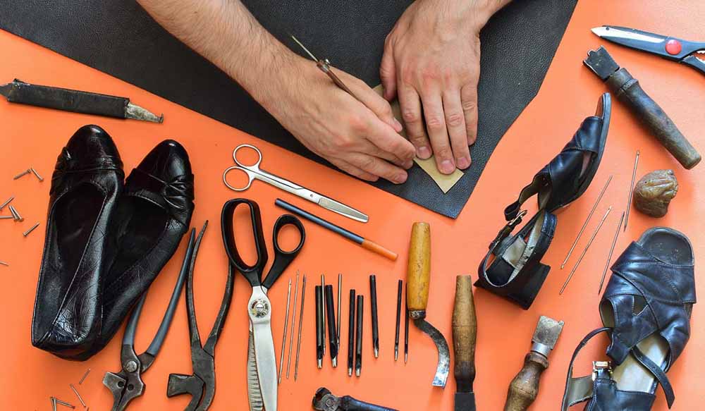 Footwear crafting tools and black leather shoes on an orange background.