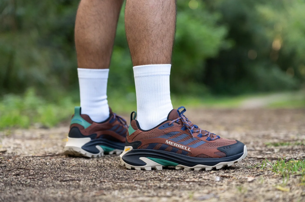 Sepatu hiking Merrell Moab Speed warna coklat dan hijau sedang dipakai di jalur tanah.